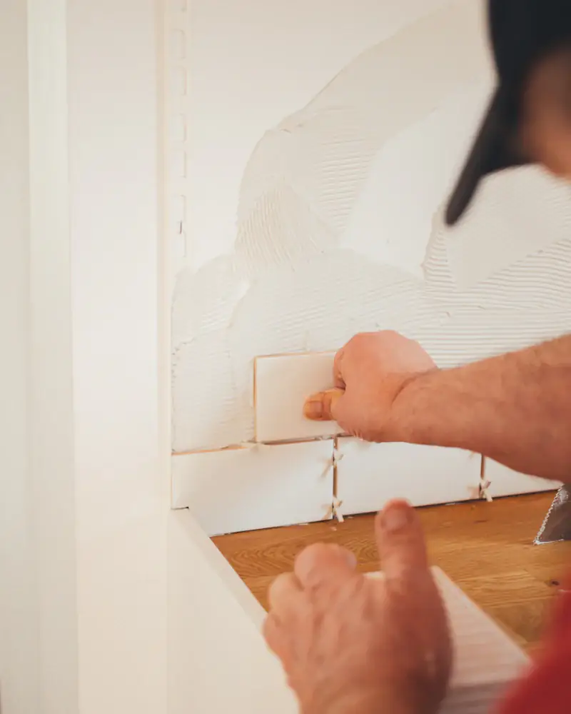 Carreleur posant un carreau de faïence blanche au mur