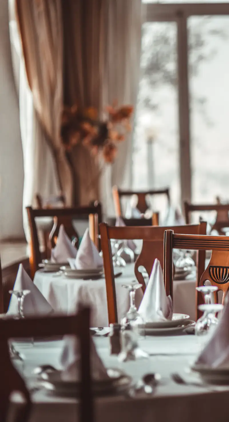 Salle du restaurant dressée, nappes blanches et grandes fenêtres